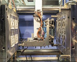 Vision/Sepro's L-shaped EOAT performs complex in-mold sequences, including rotating 90 degrees to pick finished lens assemblies from the moving half of the mold. Vision/Sepro's L-shaped EOAT performs complex in-mold sequences, including rotating 90 degrees to pick finished lens assemblies from the moving half of the mold.