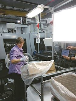 A employee inspects a lighting component after holding it up to a light table. A employee inspects a lighting component after holding it up to a light table.