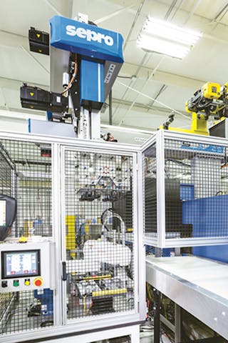 Guarding is visible around an automation cell at Vision Plastics, which molds LED lamp components. Behind the guarding is a small SCARA robot that is used to position inserts for the Cartesian robot to pick up and place in the mold.