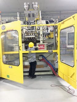 Quality assurance: An employee conducts routine maintenance on a blow molding machine. Quality assurance: An employee conducts routine maintenance on a blow molding machine.