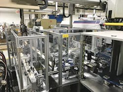 Two integrated injection molding machines produce top and bottom housings for a specialty container. The two components are brought together via robotic end-of-arm tooling and placed on reorientation fixtures to accommodate hot-stamp decorating, assembly and validation processes. Two integrated injection molding machines produce top and bottom housings for a specialty container. The two components are brought together via robotic end-of-arm tooling and placed on reorientation fixtures to accommodate hot-stamp decorating, assembly and validation processes.