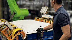A worker reaches into a work cell that includes a Fanuc CR-35iA collaborative robot.