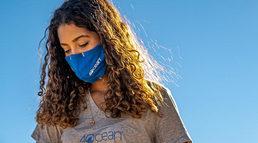 A woman sports a 4ocean shirt, face mask and face-mask frame. The products are part of the company's portfolio, with proceeds of sales spent on ocean cleanups.