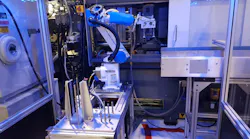 A robot from Shibaura, the company formerly known as Toshiba, operates at an injection molding machine.