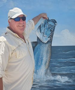 Rick Finnie strikes a creative pose in front of a painting of a fish.