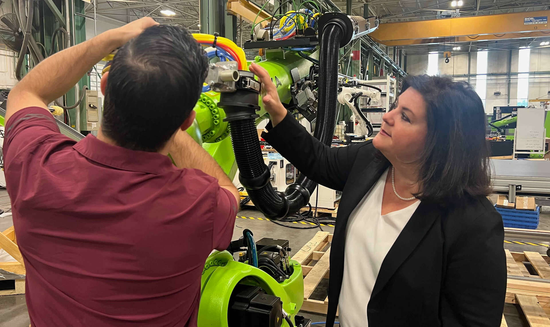 Engel North America's President Vanessa Malena watches a technician make adjustments to the end-of-arm-tool on an Engel robot arm.