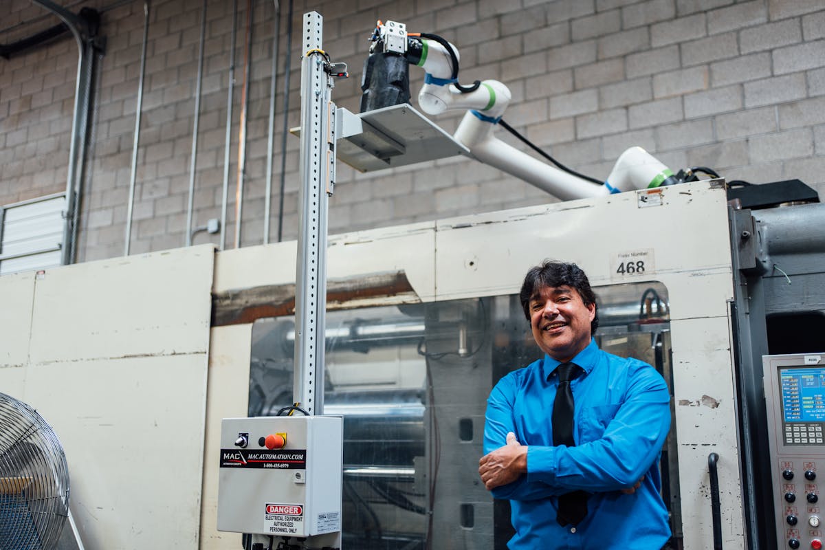Jeff Galindo, Icon Injection Molding&apos;s executive operations specialist, stands next to an injection molding machine equipped with a Fanuc collaborative robot from Formic.