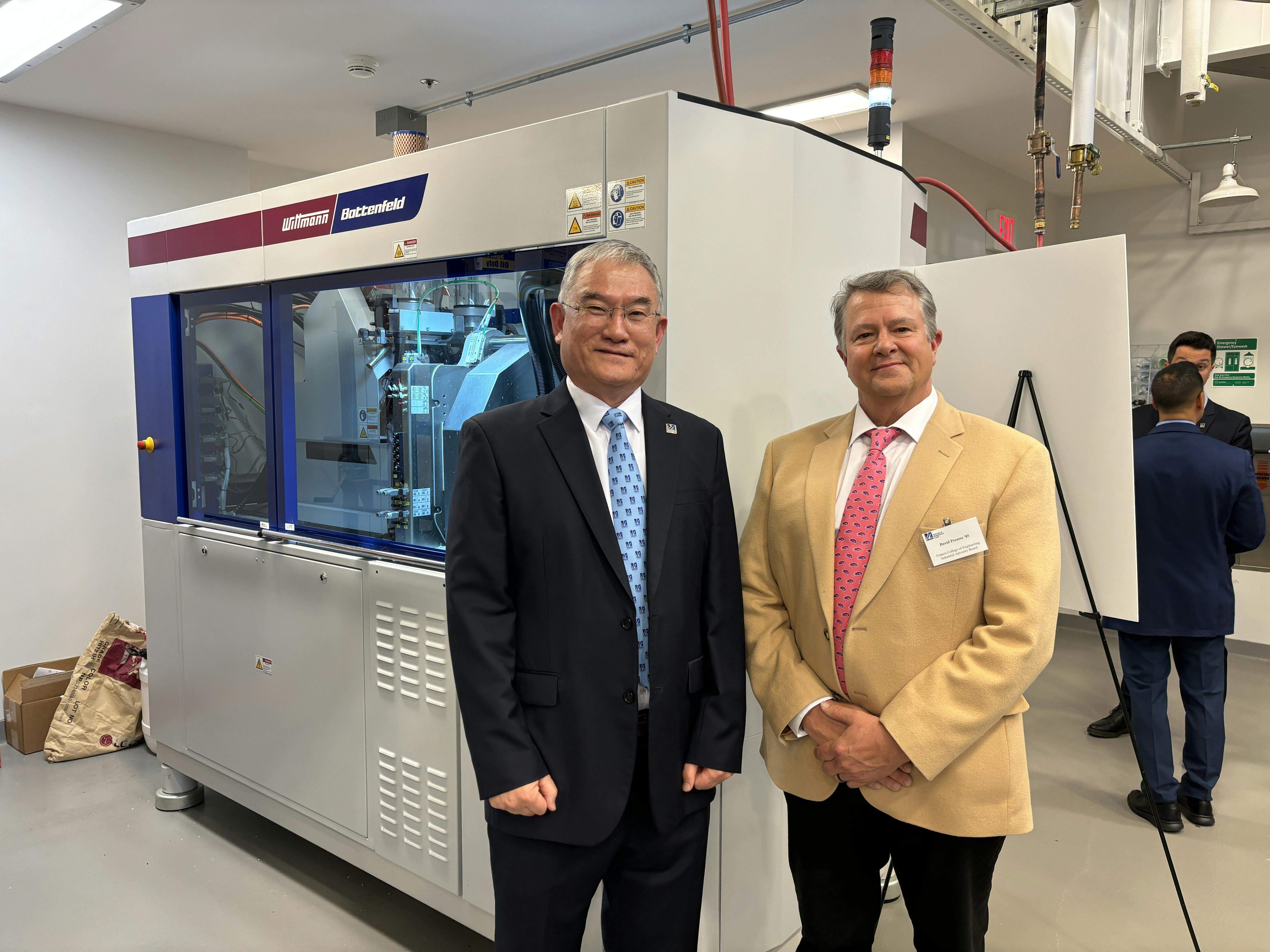 WITTMANN USA President David Preusse, right, and Ho-Seon Jin, Eli Lilly senior director-engineering, stand in front of the Wittmann MicroPower injection molding machine that was part of the work cell donated to the University of Massachusetts Lowell.