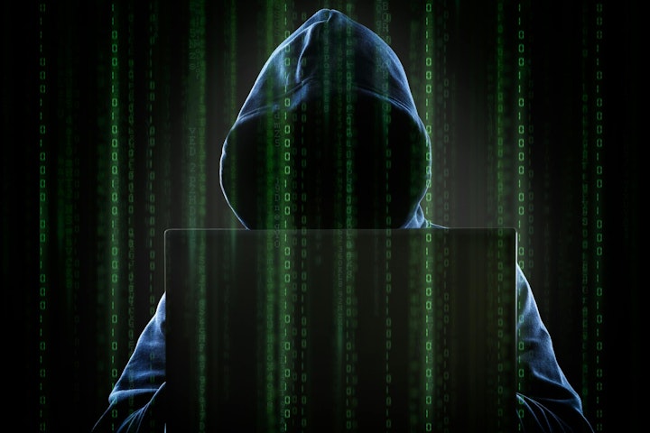 A hooded hacker at a computer.