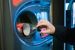 A person returns a plastic bottle to a recycling receptacle. A person returns a plastic bottle to a recycling receptacle.