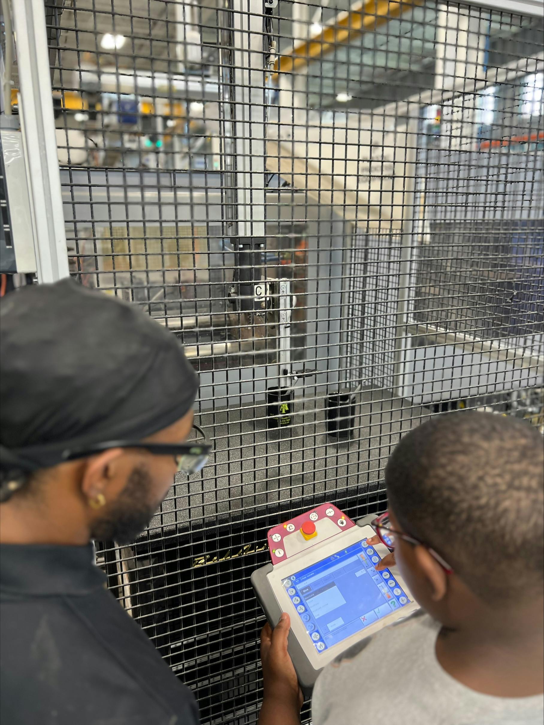 Molding Kids for Success program participants learn injection molding basics including how to operate a digital controller. Anthony Oliver, left, supervises a student&rsquo;s lesson.