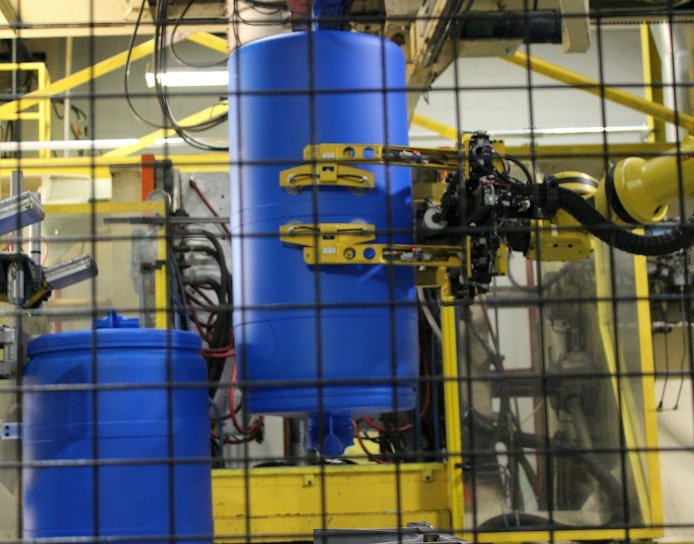 A robot provided by Minatech interfaces with a blow molding machine producing drums at Greif.