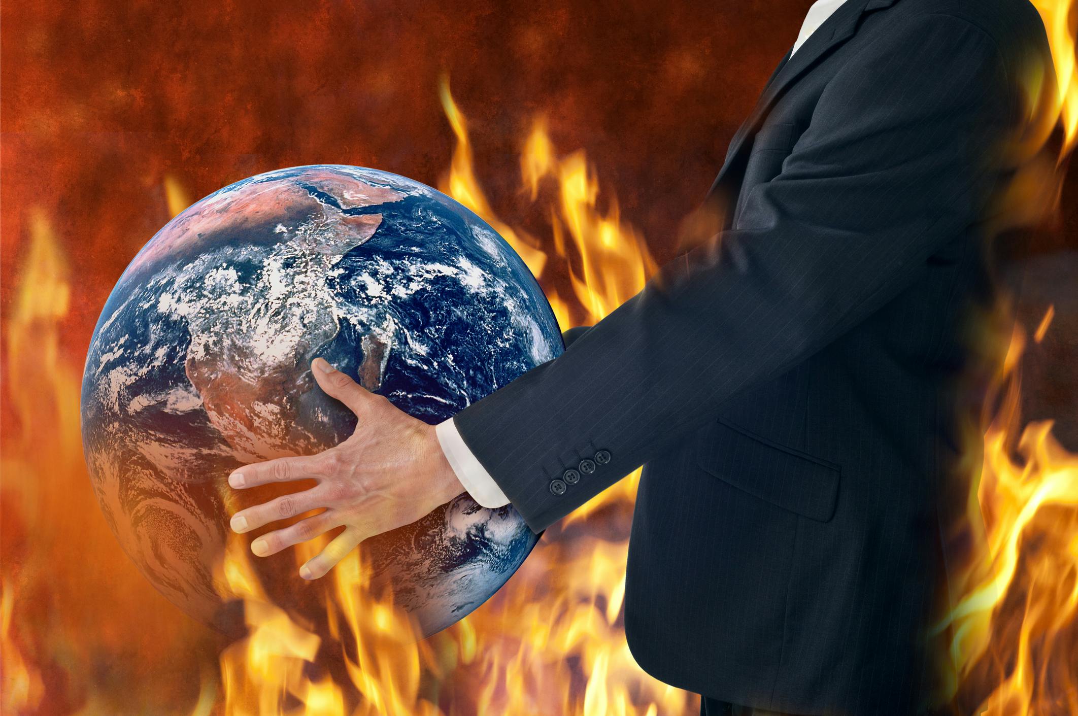 Businessman holds a globe as fires burn around him