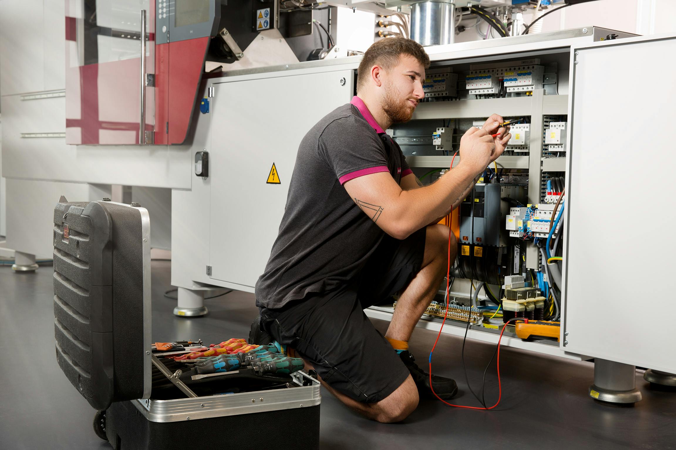 A technician crouches beside Wittmann equipment. Like other OEMs, Wittmann is working to make its machines easier to use, with tools that will help processors better spot trends that could indicate future maintenance needs.