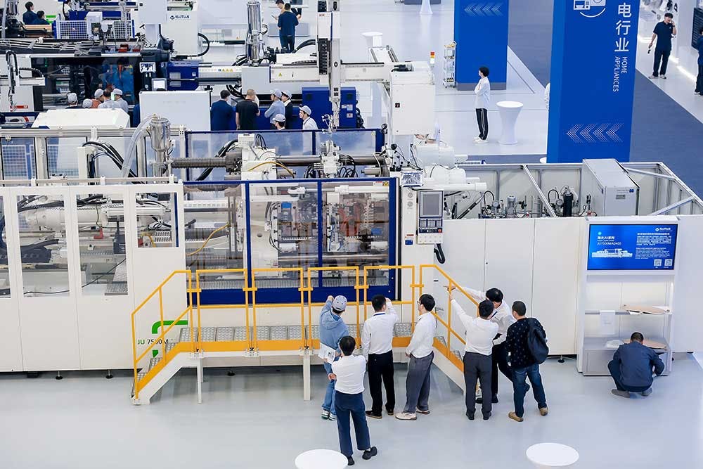 A group of people watch a part being produced on a Haitian injection molding machine.