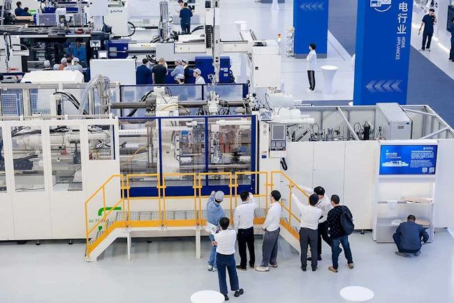 A group of people watch a part being produced on a Haitian injection molding machine.