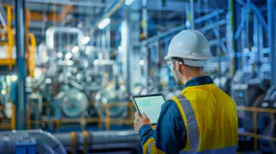 Man in a hard hat with a tablet watches a manufacturing line.