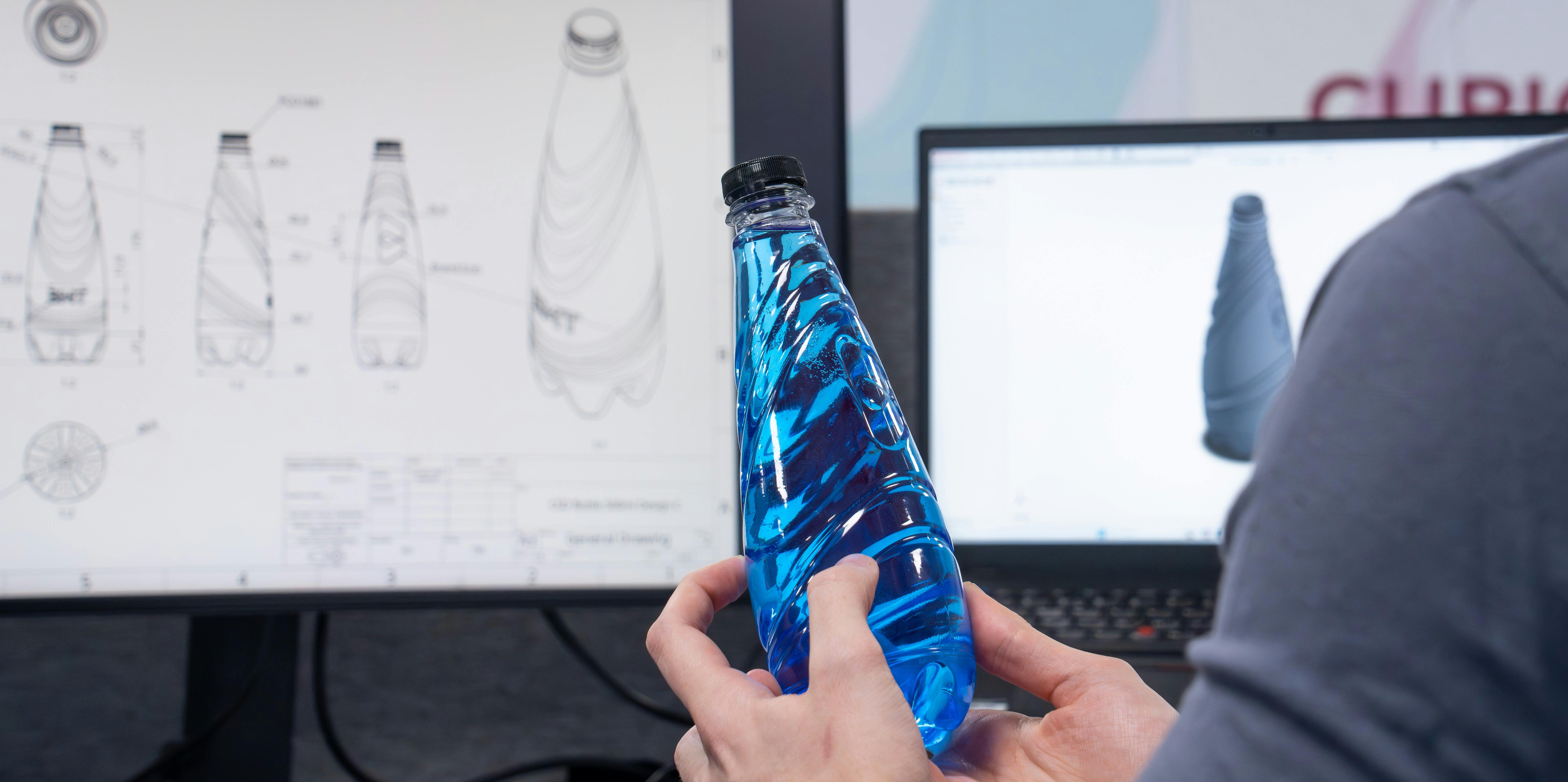Hands hold a blue bottle in front of a screen showing simulations of the bottle design.