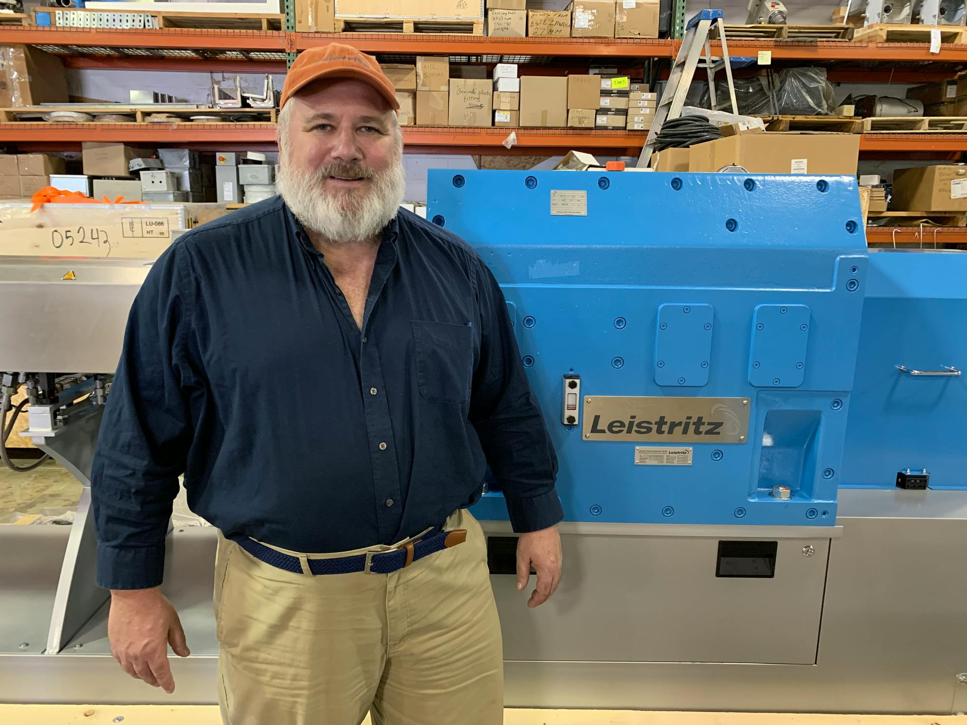 Charlie Martin, bearded man in blue shirt, standing in front of a Leistritz extruder.