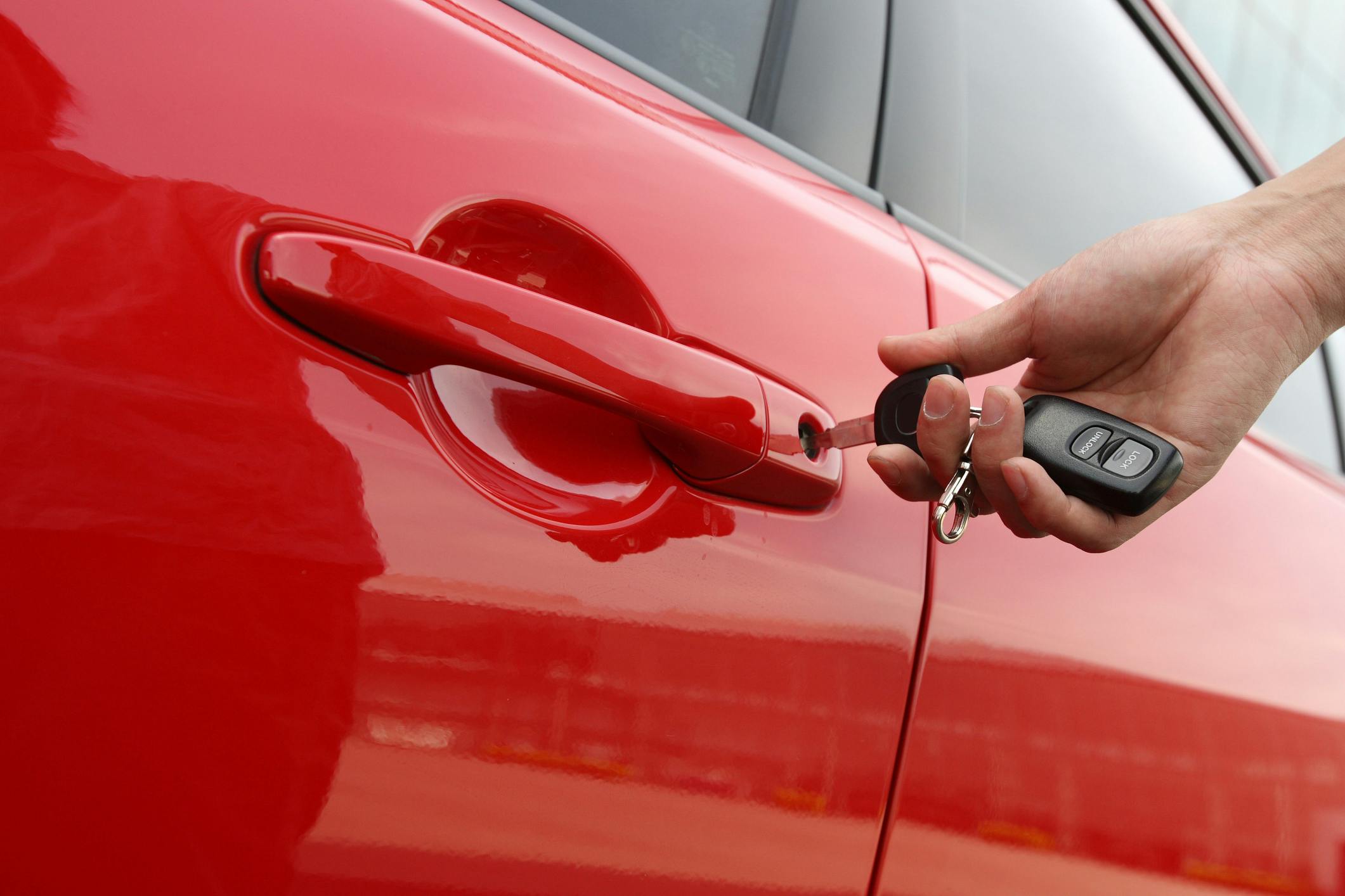 A hand inserts a key into a red car door.