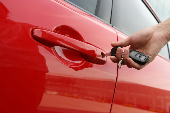 A hand inserts a key into a red car door.