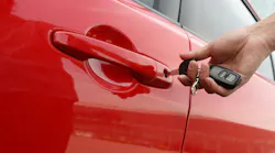A hand inserts a key into a red car door.