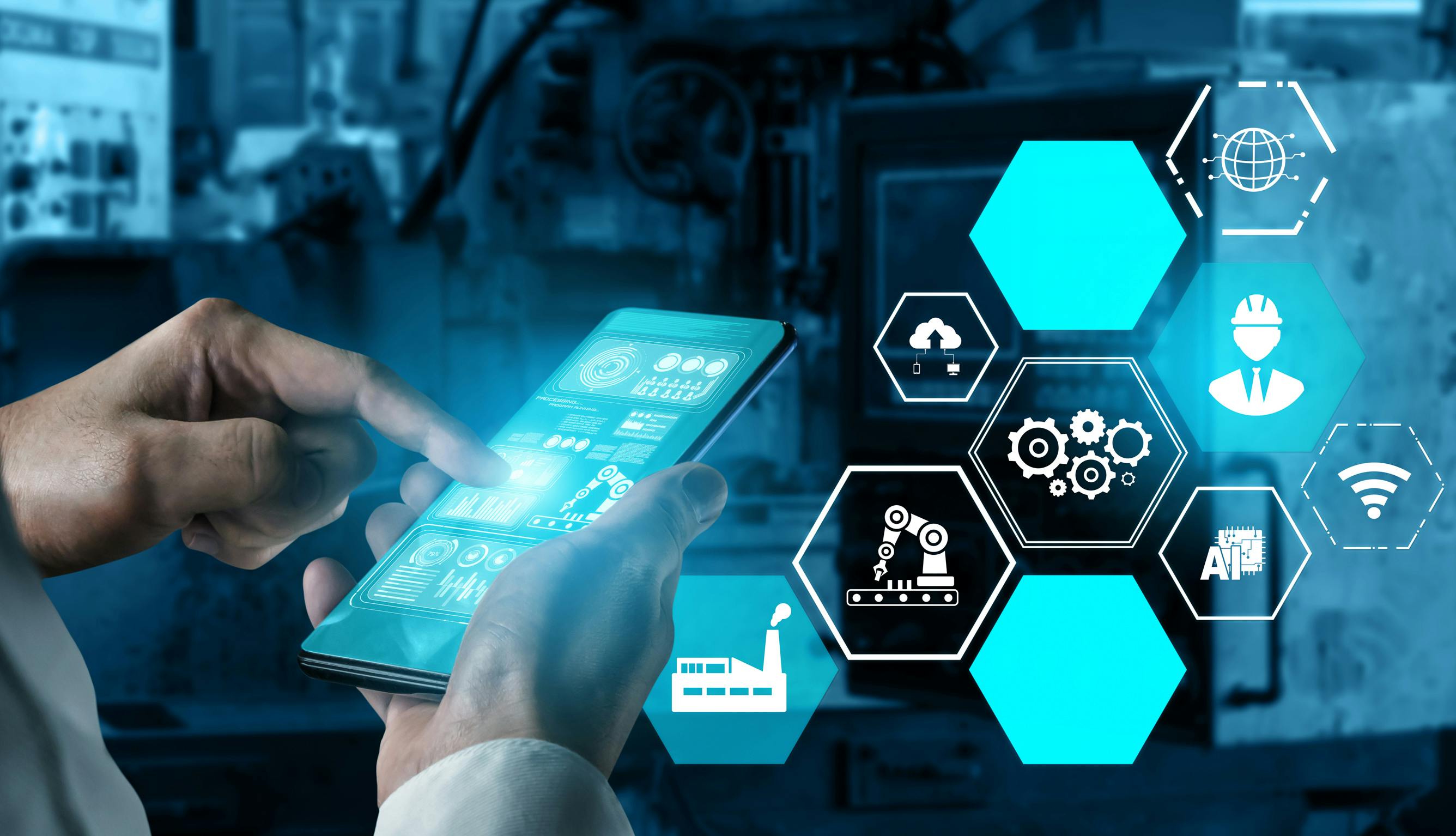 A hand operates a screen controlling elements of a smart factory.