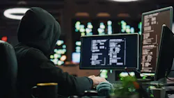 Hacker in a hoodie works on a computer.