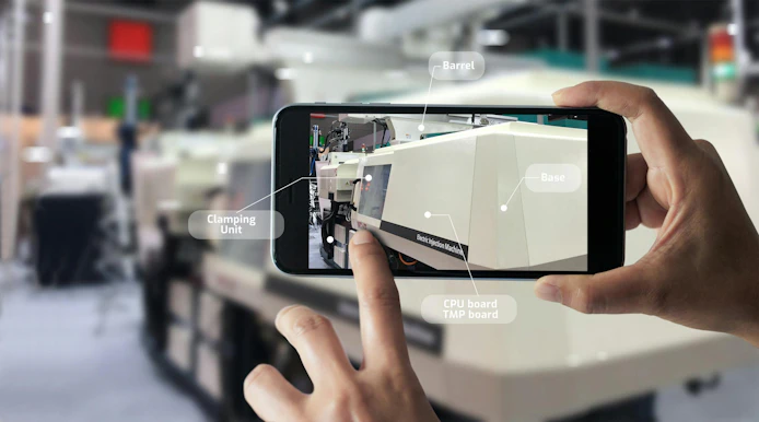 A smartphone shows various parts of an injection molding machine to a user.