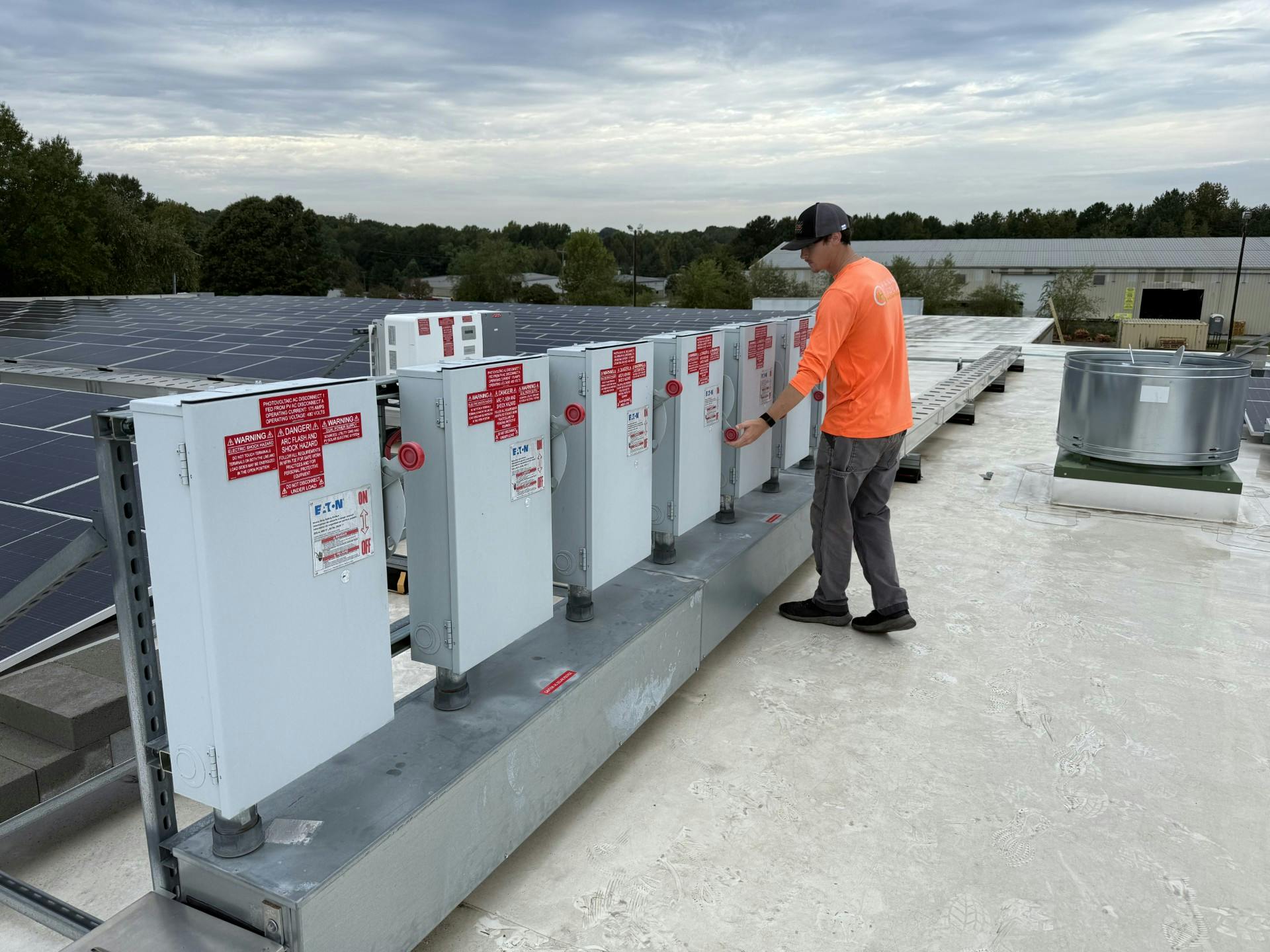 Worker on roof of a plant with solar energy system on a partly cloudy day.
