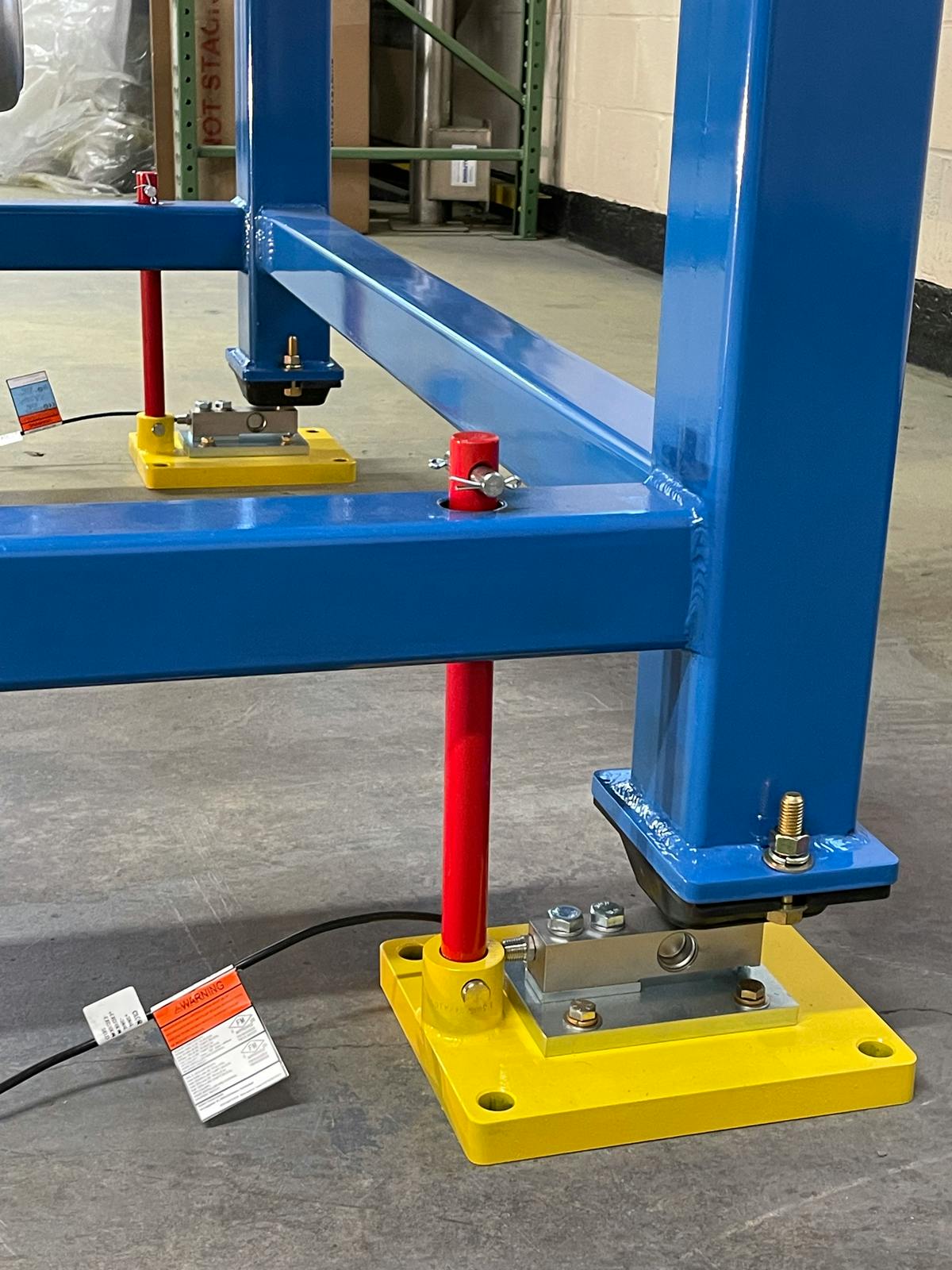 Red failsafe bars anchor a blue bulk bag unloader to the floor.