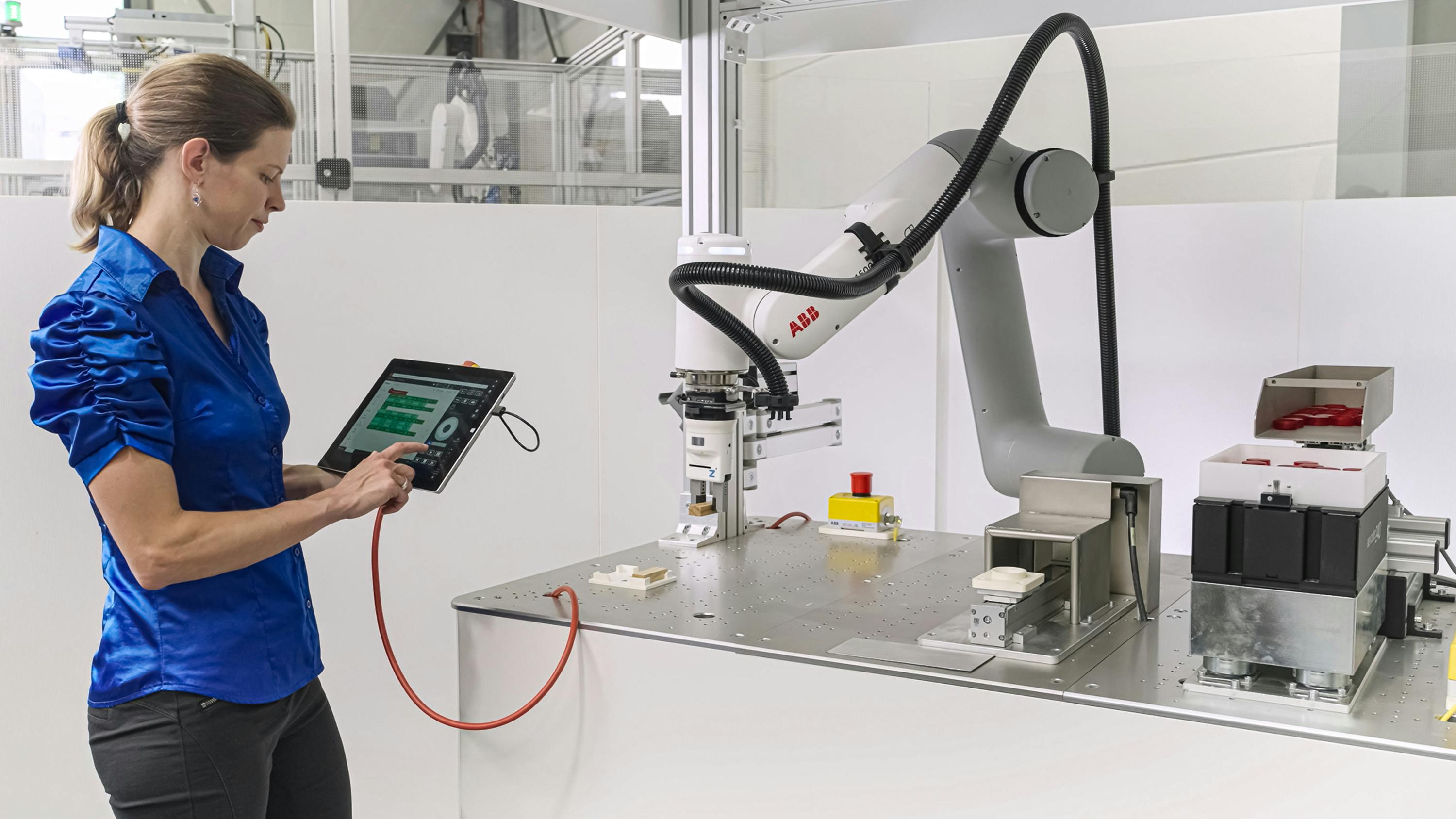 A woman operates a cobot using an E-Device and a tablet