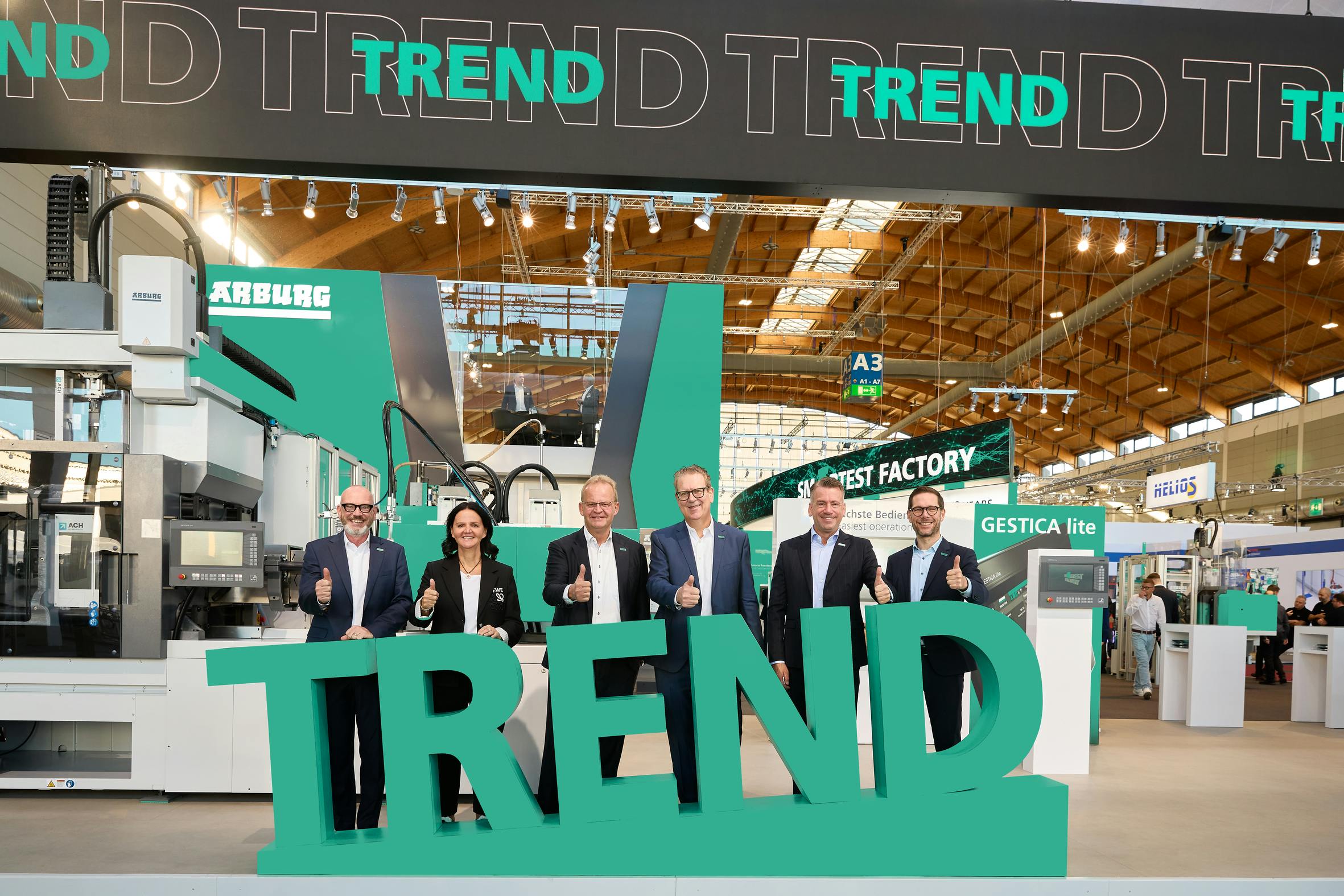 Arburg's management team poses behind a green sign for the 'Trend' machine