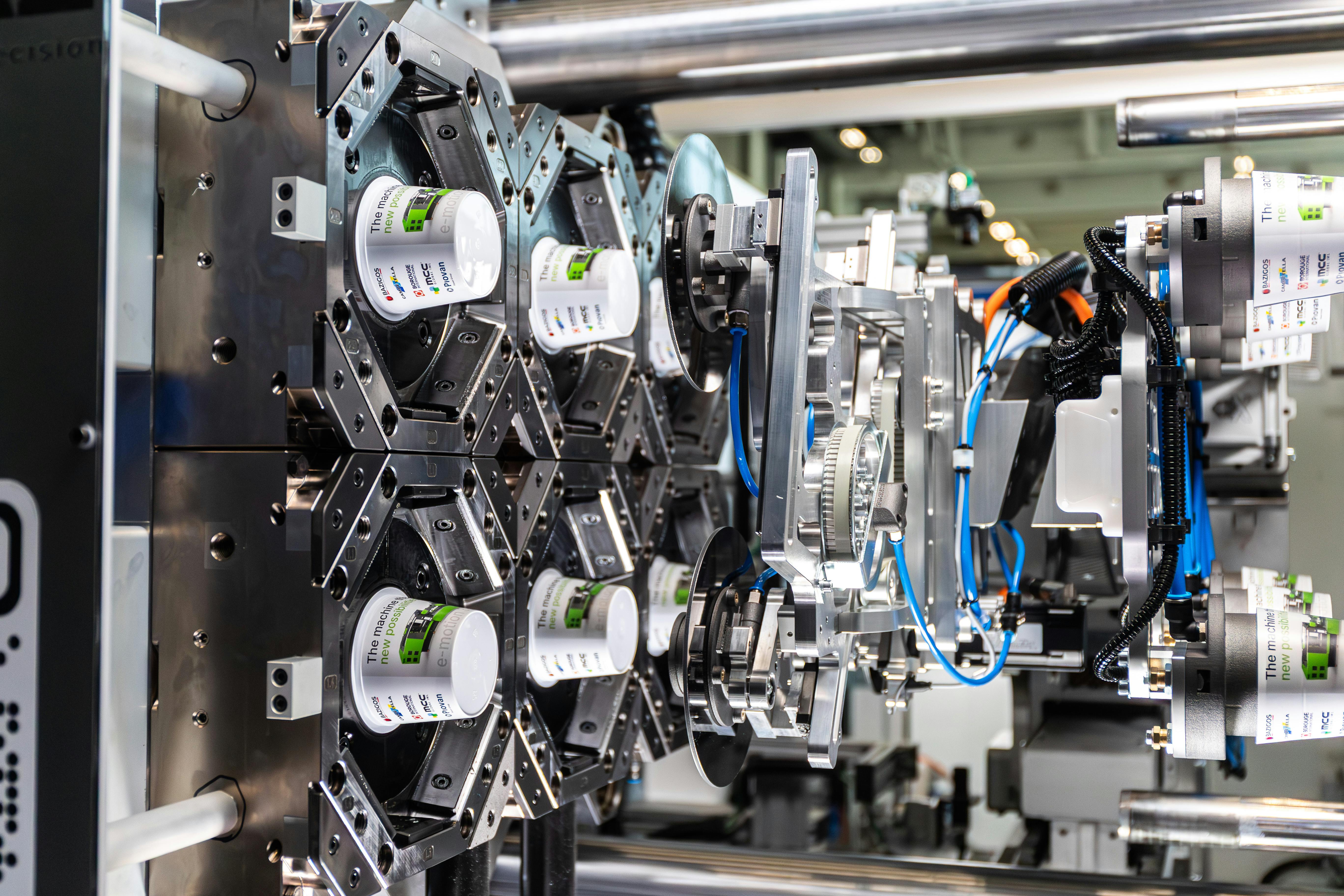 An injection mold opens with molded yogurt cups inside