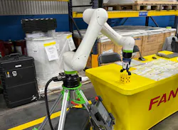 A yellow Fanuc robot reaches for a large die at a display table