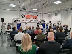 People listen to a speaker standing in front of a Bay Plastics Machinery banner.